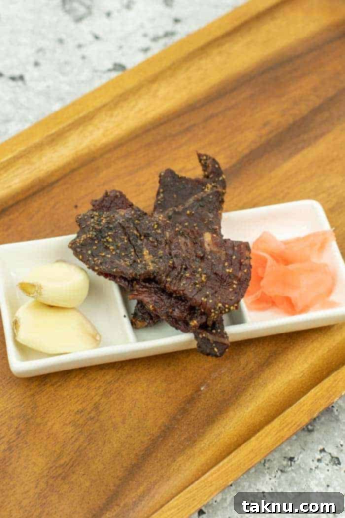 Kikkoman Glazed Teriyaki Beef Jerky 2 Teriyaki Beef jerky on dish with ginger and garlic backed by wood cutting board