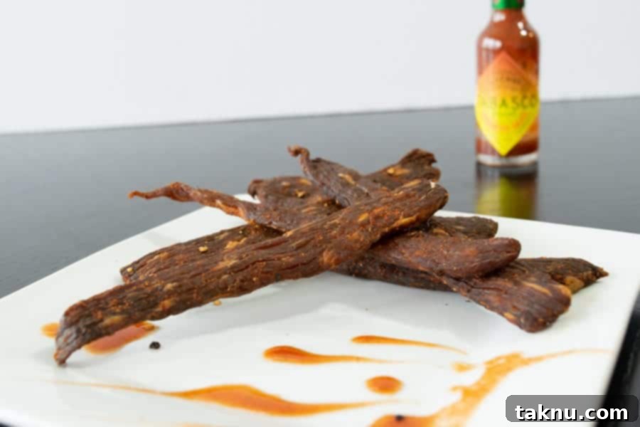 Finished Habanero Tabasco jerky strips beautifully arranged on a plate alongside a Tabasco bottle, illustrating the enticing final product.