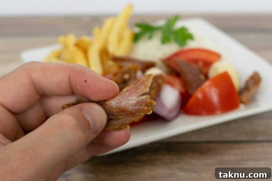 Finished turkey jerky bent showing white fibers with plate of tomatoes and fries in the background
