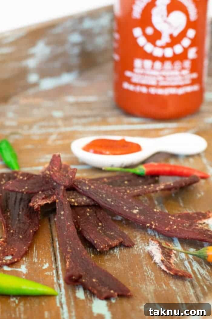 Sriracha Deer jerky on wood tray with sriracha bottle and fresh peppers, showcasing the finished product