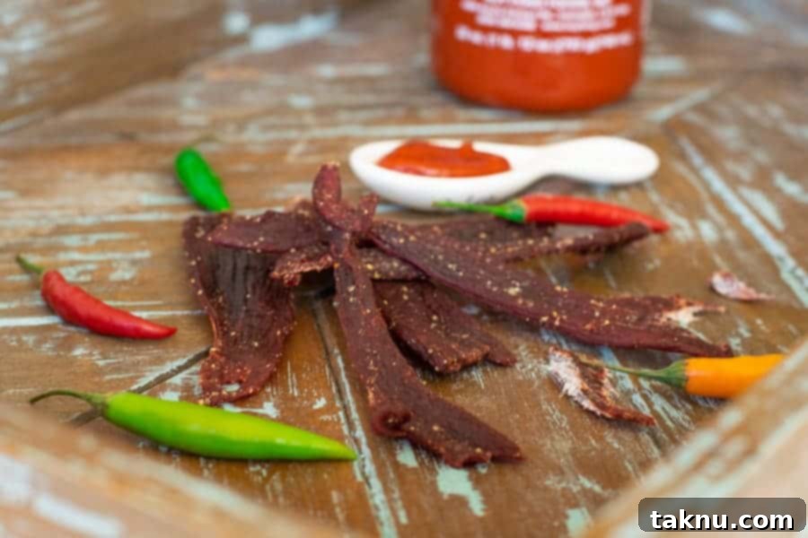 Sriracha deer jerky displayed on a cutting board with fresh peppers and sriracha sauce bottles