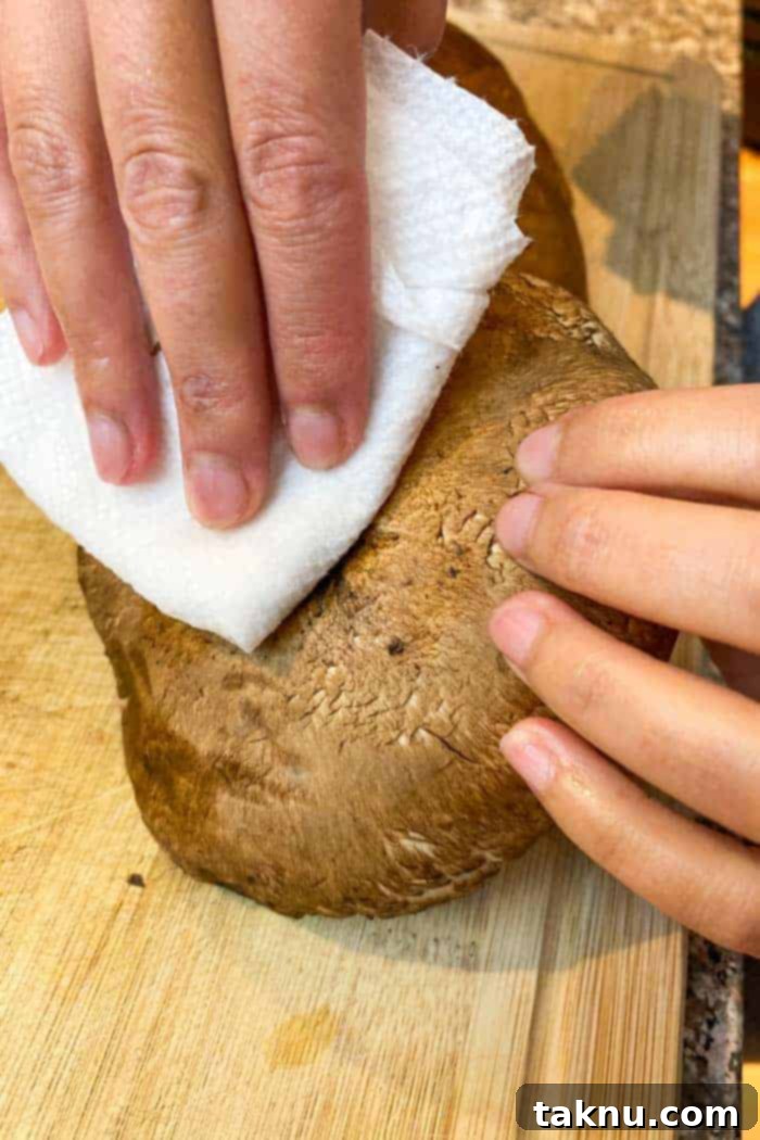 Hand wiping dirt from Portobello mushroom with wet paper towel