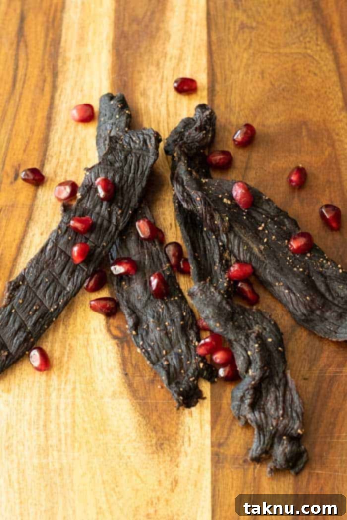Pomegranate deer jerky on cutting board, showcasing the beautiful reddish-brown strips ready for snacking.