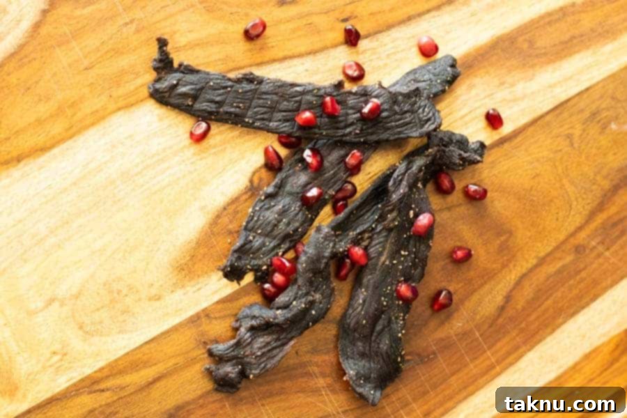 Pomegranate Deer Jerky arranged on a cutting board, garnished with fresh pomegranates, highlighting its vibrant flavor.