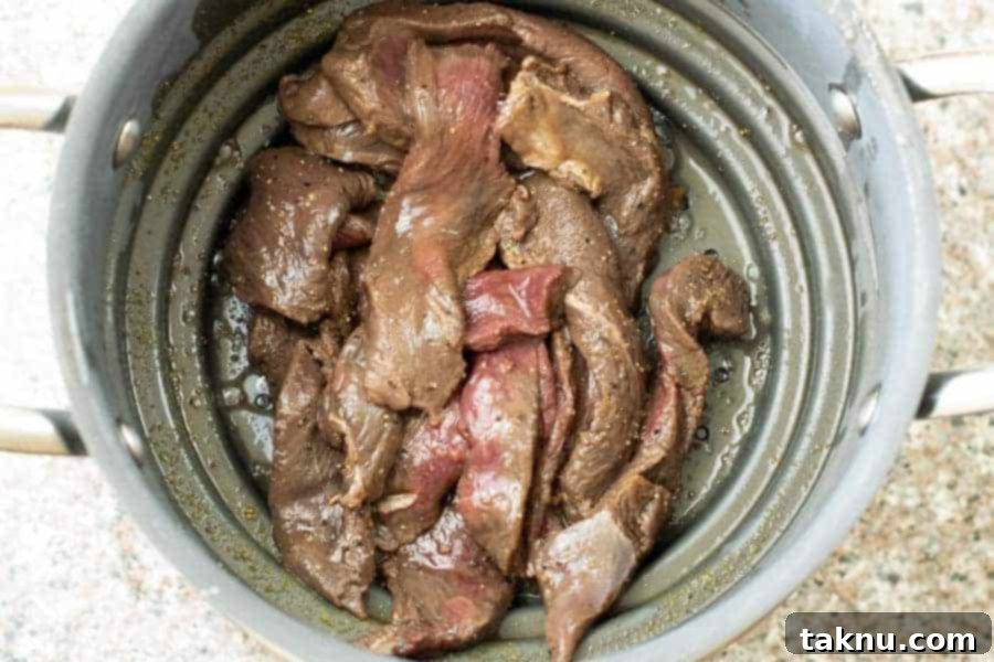 Deer jerky strips strained in a colander, removing excess marinade.