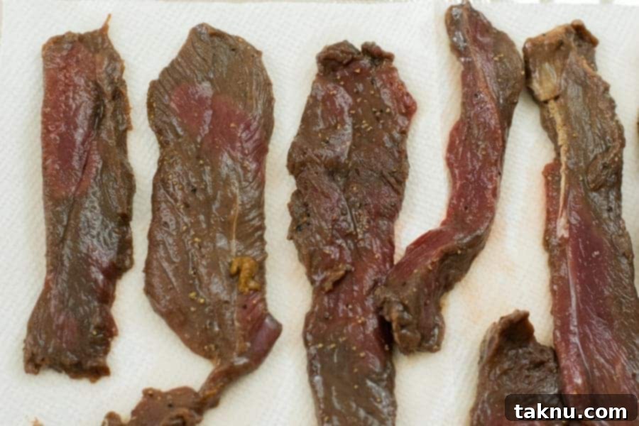 Deer jerky strips laid out on paper towels and being patted dry to remove surface moisture.
