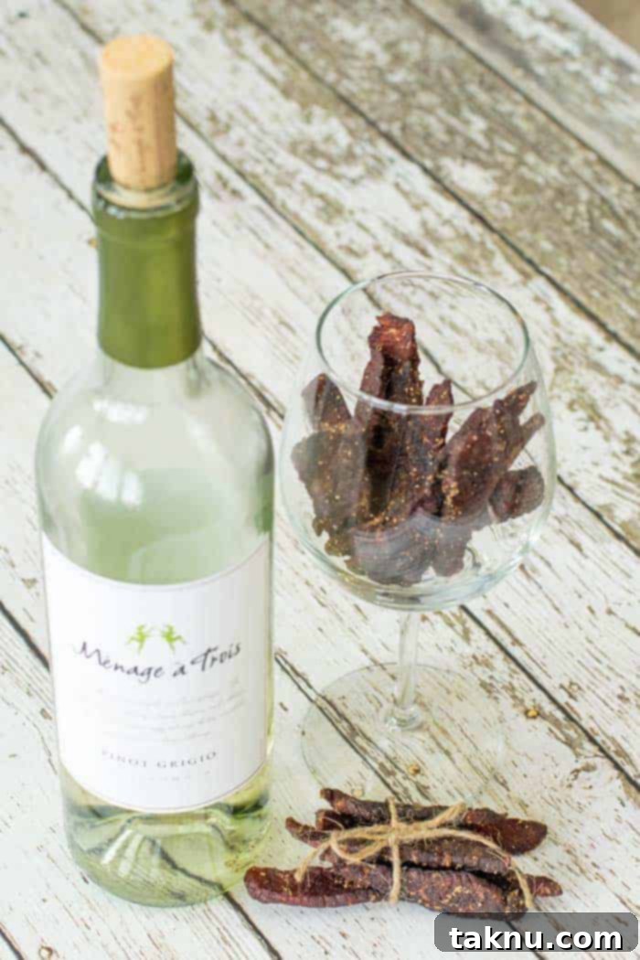 Vintner's Mash Beef Jerky 2 Bottle of white wine on wooden table next to a wine glass with beef jerky inside
