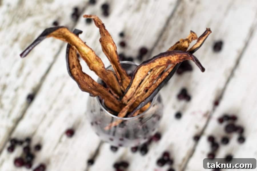 Homemade blueberry eggplant jerky stored in a glass jar, with fresh blueberries scattered on a white table