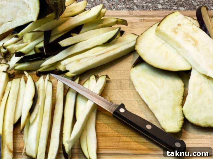 Sharp knife on a wooden cutting board with thinly sliced eggplant, ready for preparation
