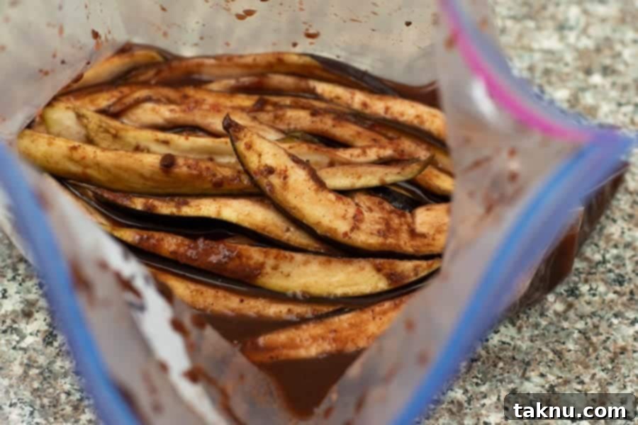 Eggplant slices inside a ziplock bag, with the rich plum-colored marinade being poured over them