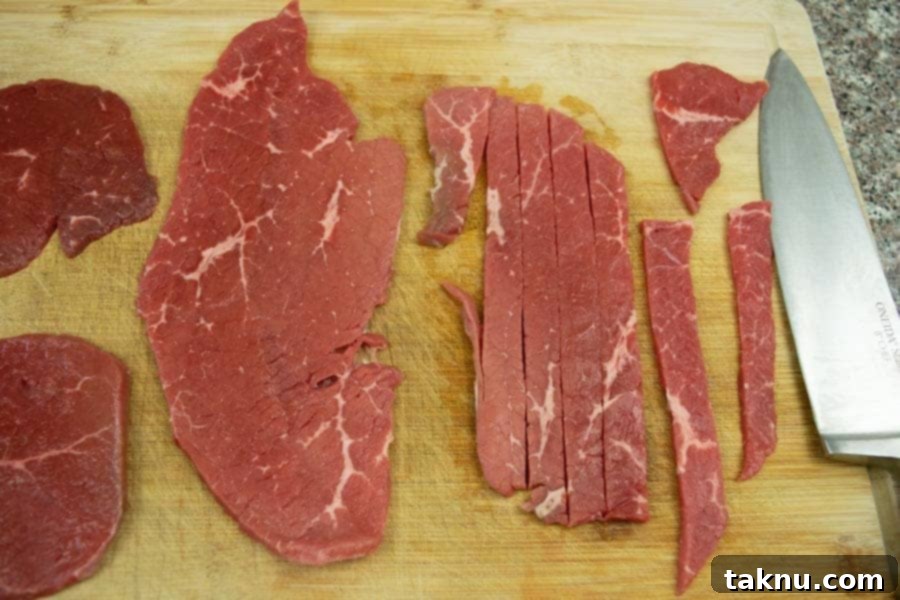 Beef top round sliced thin on cutting board with knife
