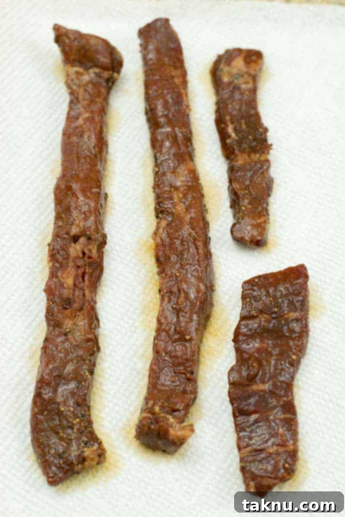 Gunslinger's Jerky 11 Patting marinated jerky strips dry with paper towels to remove excess moisture before dehydrating.