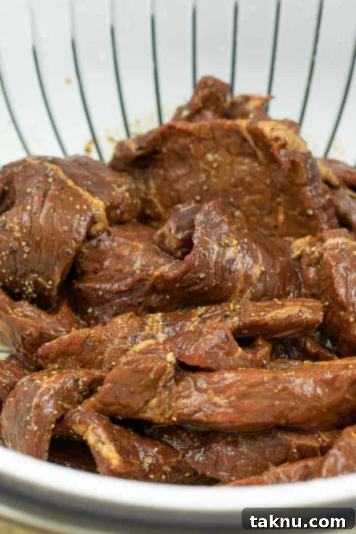 Gunslinger's Jerky 10 Jerky strips straining in a colander, removing excess marinade for optimal drying.