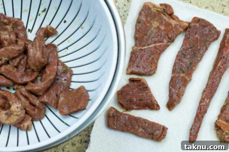 Marinated jerky strips in a colander and on paper towels