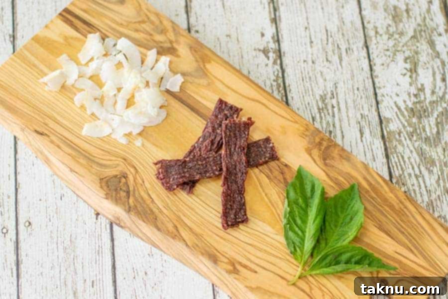 coconut ground beef jerky on cutting board with coconut shavings and fresh basil leaves