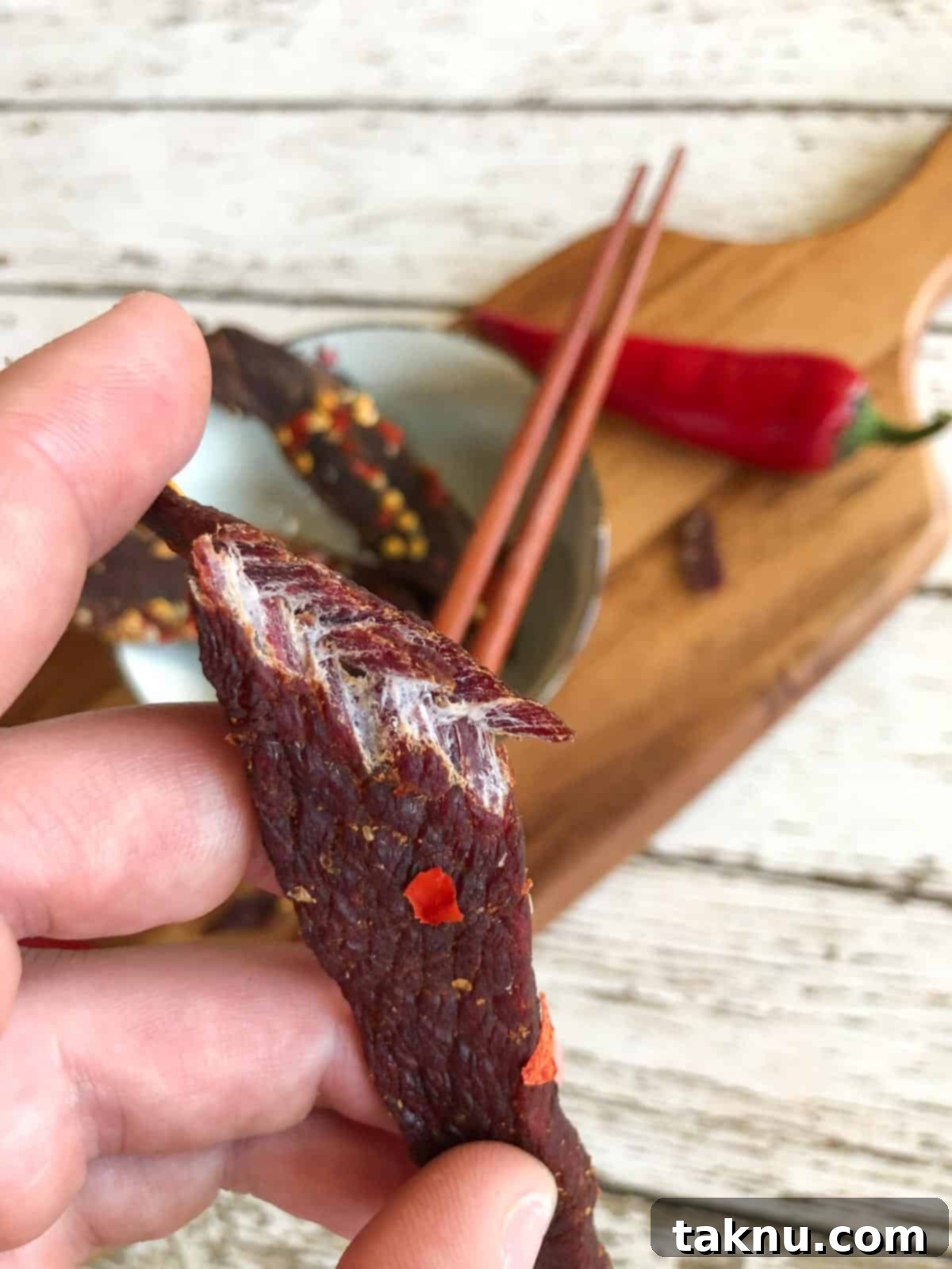 Sesame Glazed Venison Strips 8 venison jerky bent in half showing it is finished drying by the white fibers and cutting board in background