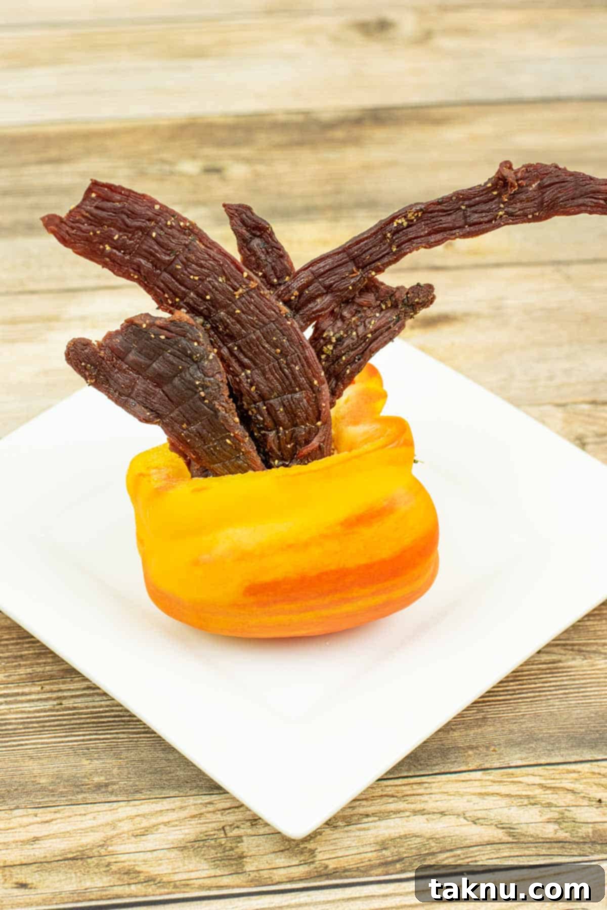 Zesty Beef Jerky 2 Tangy beef jerky coming out of an orange bell pepper on a white plate, highlighting its vibrant flavor