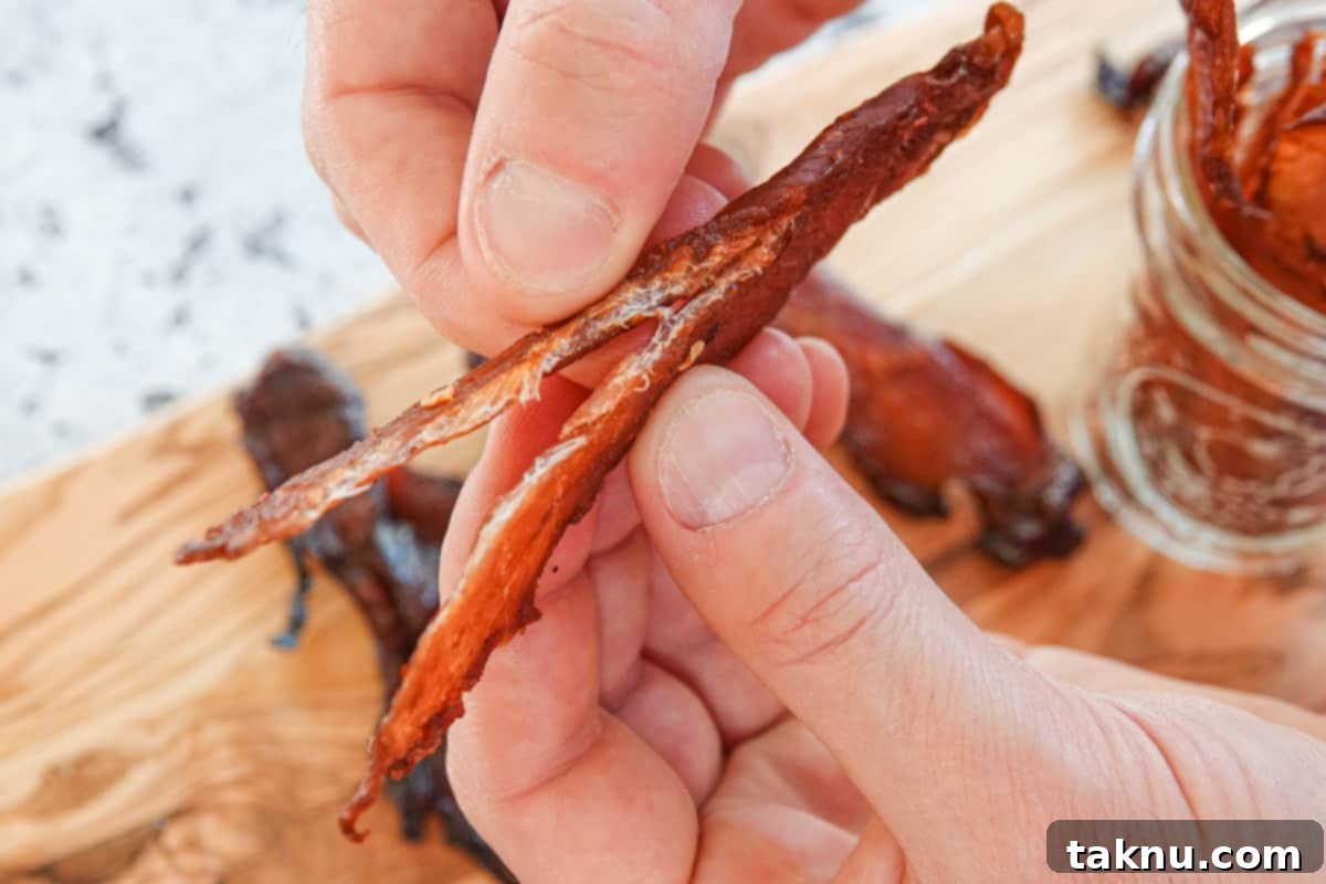 Chicken Jerky 8 chicken jerky being ripped in half showing it's finished drying. Cutting board in background