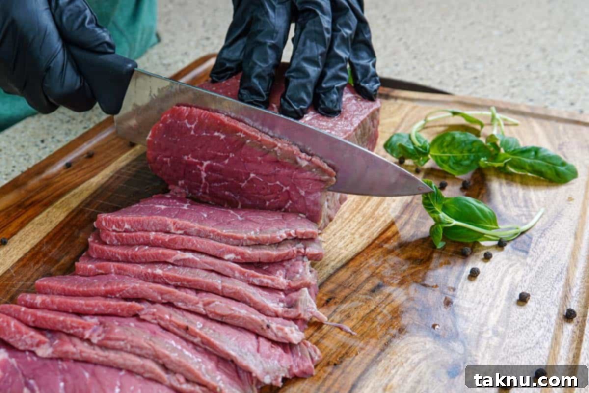 Slicing meat for beef jerky on cutting board with knife