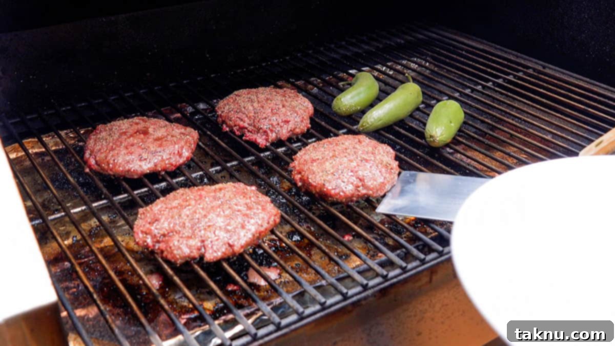 Hamburgers smoking on a grill, surrounded by jalapeños, with wisps of smoke visible.