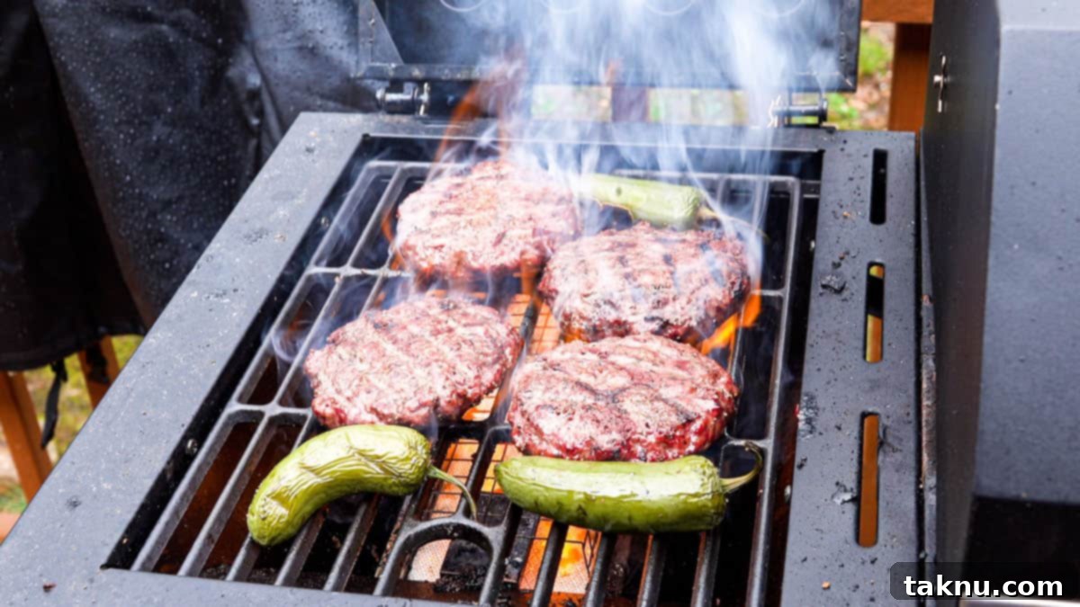 Hamburgers searing on a hot grill with grill marks, alongside grilled jalapeños.