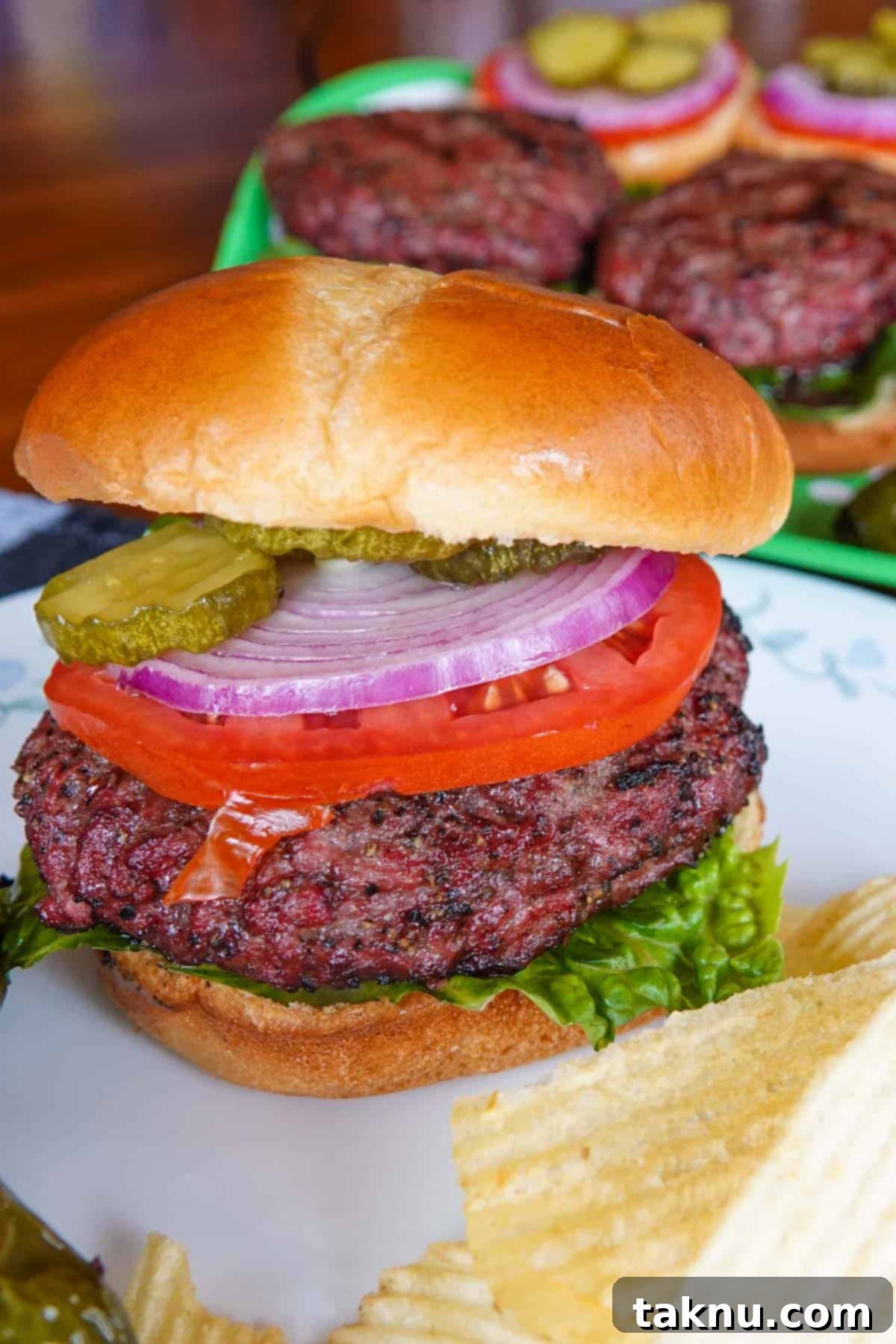 A perfectly cooked smoked hamburger on a plate, with additional blurred burgers in the background, ready to be served.