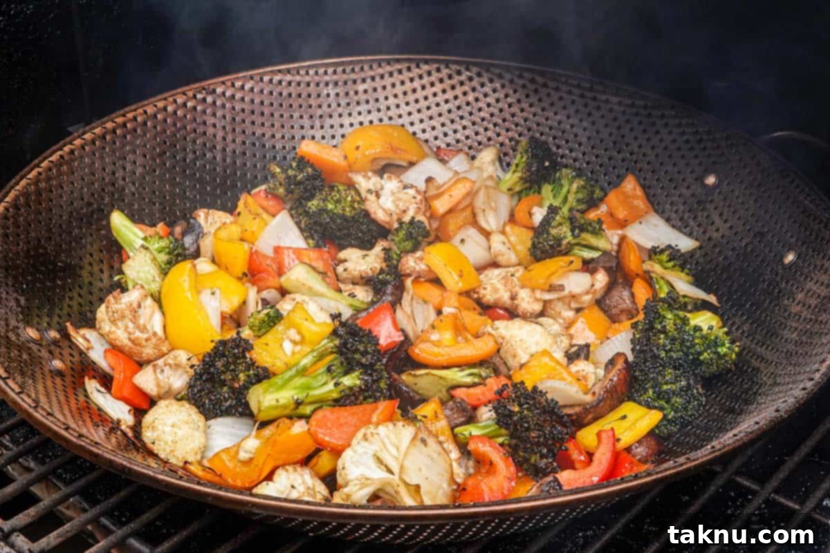 Colorful seasoned vegetables cooking in a metal grill basket inside a smoker, with visible smoke providing flavor.