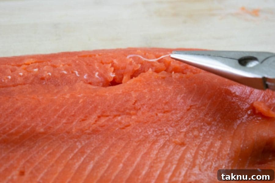 Detailed shot of hands carefully removing pin bones from a salmon fillet with needle-nose pliers
