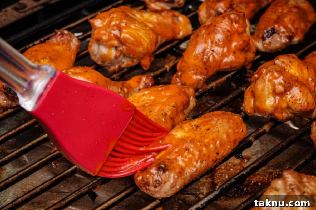 Irresistibly Crispy Smoked Chicken Wings 8 A hand brushing wing sauce onto golden-brown smoked chicken wings on a grill grate.