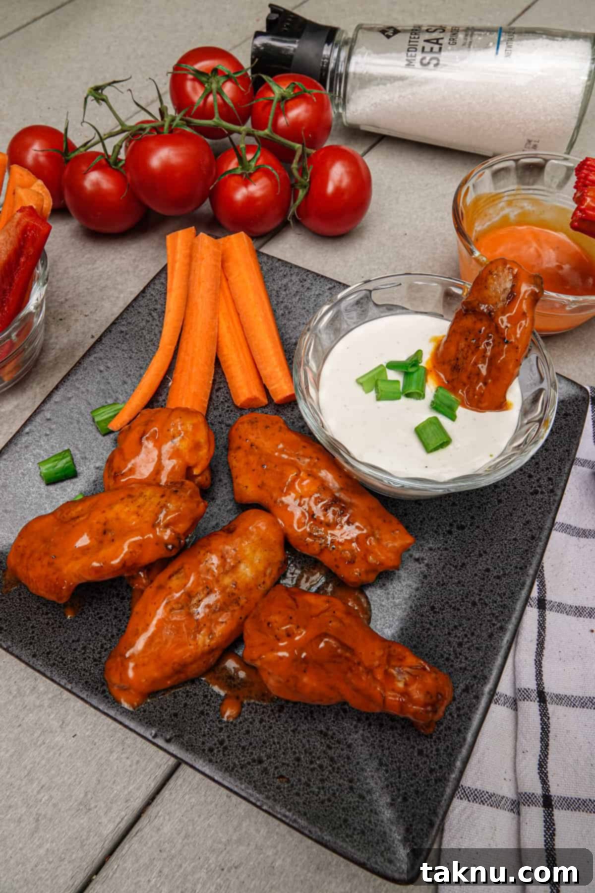 Irresistibly Crispy Smoked Chicken Wings 9 A large platter of crispy smoked chicken wings, garnished with fresh carrots and tomatoes, with a side of creamy ranch dressing.