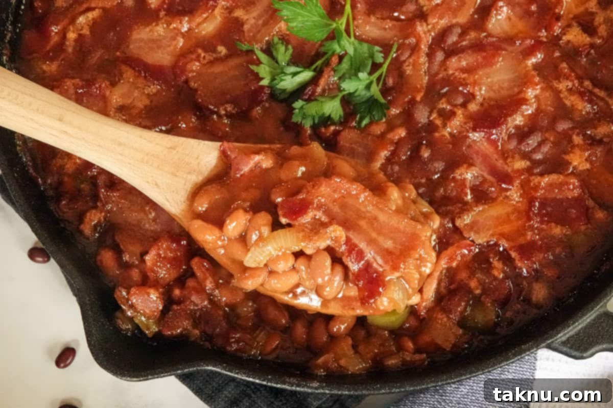 Smoky Bacon Baked Beans 6 A serving spoon dishing out a generous portion of hot, smoky baked beans from the cast iron pan.