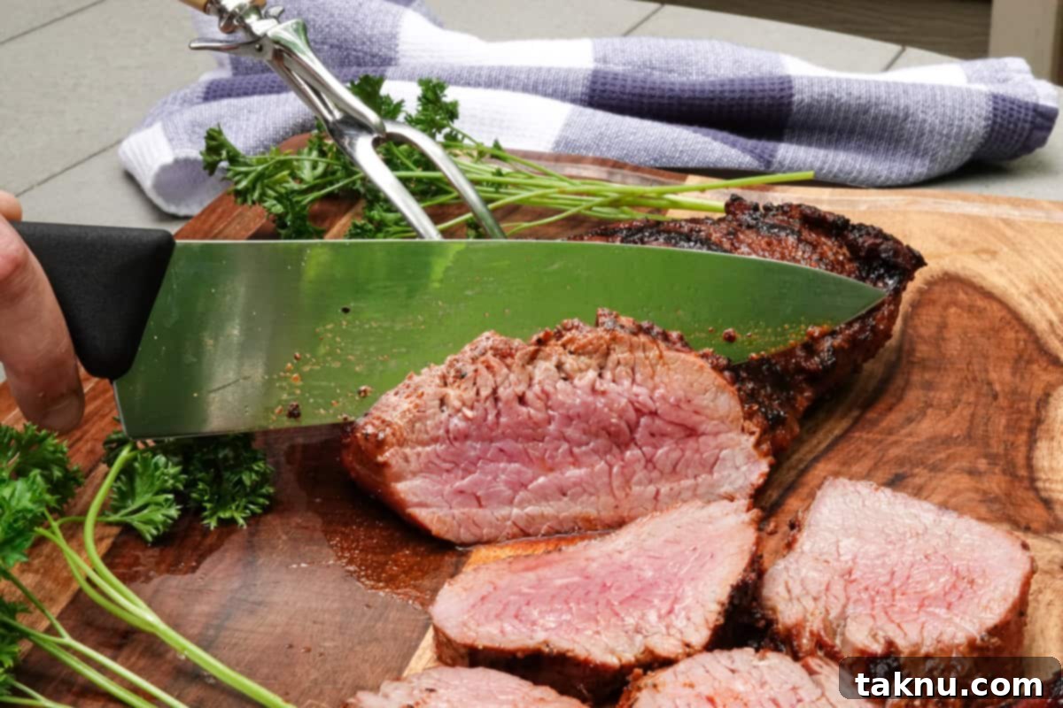 A chef's knife expertly slicing a cooked tri-tip steak against the grain on a cutting board.