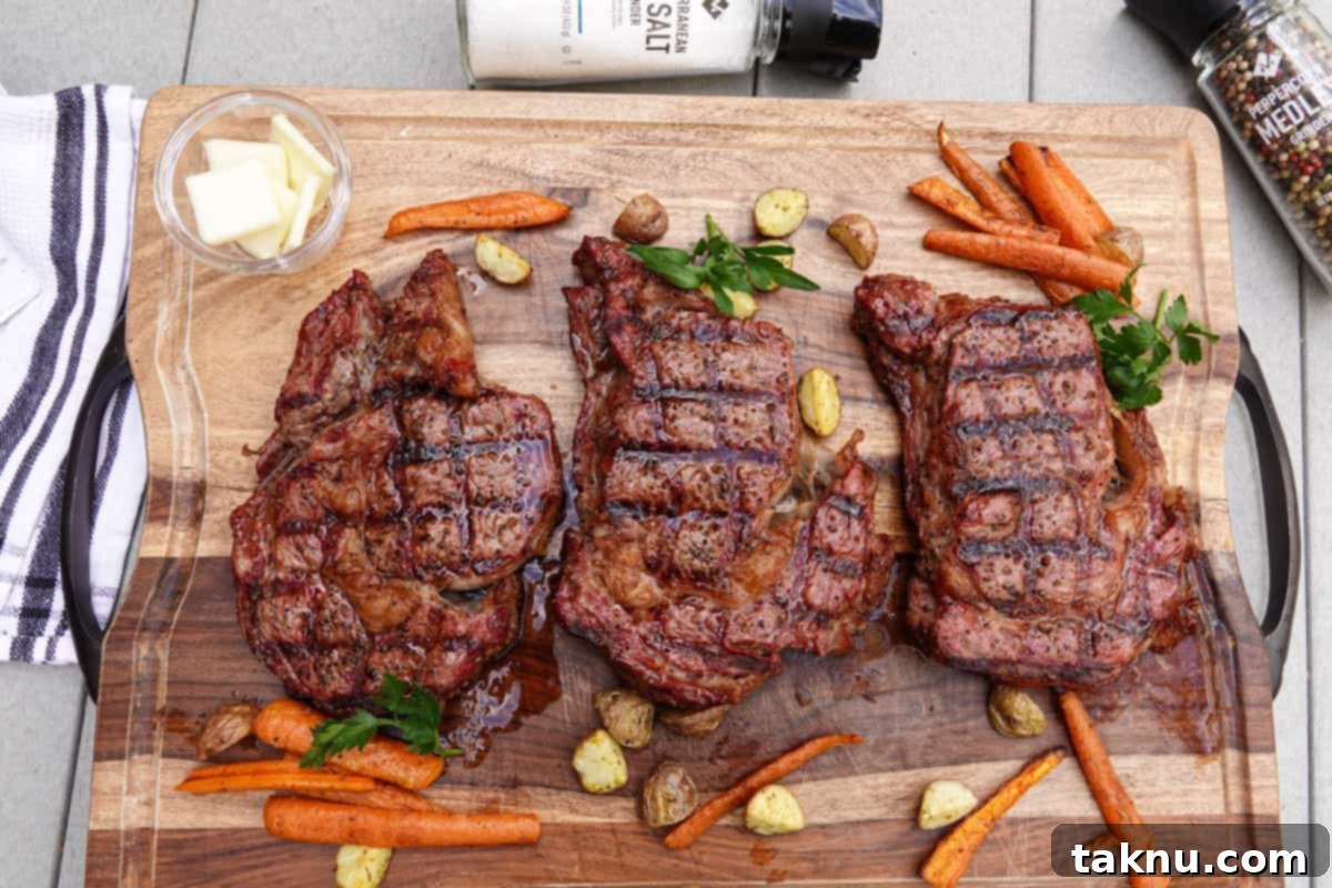 Ultimate Smoked Ribeye 9 Three perfectly cooked ribeye steaks on a cutting board with roasted vegetables, ready to be enjoyed.