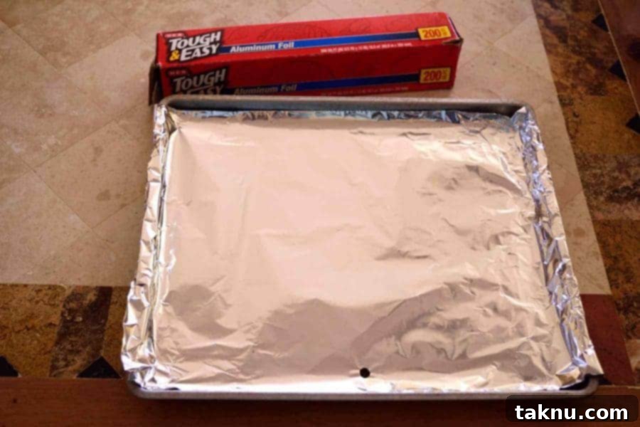 Crafting Smoked Beef Jerky 8 Close-up of a smoker's drip pan being covered with aluminum foil for easy cleaning.