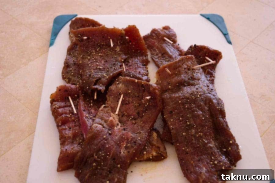 Crafting Smoked Beef Jerky 10 Garlic black pepper beef jerky strips pierced with toothpicks, ready to be hung in the smoker for drying.